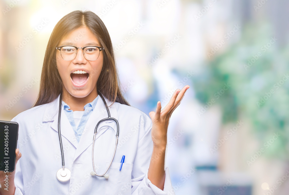 Young asian doctor woman holding smartphone over isolated background very happy and excited, winner expression celebrating victory screaming with big smile and raised hands