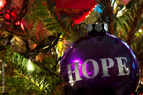 A purple bulb Christmas ornament hanging on a Christmas tree with HOPE in silver etched on it.