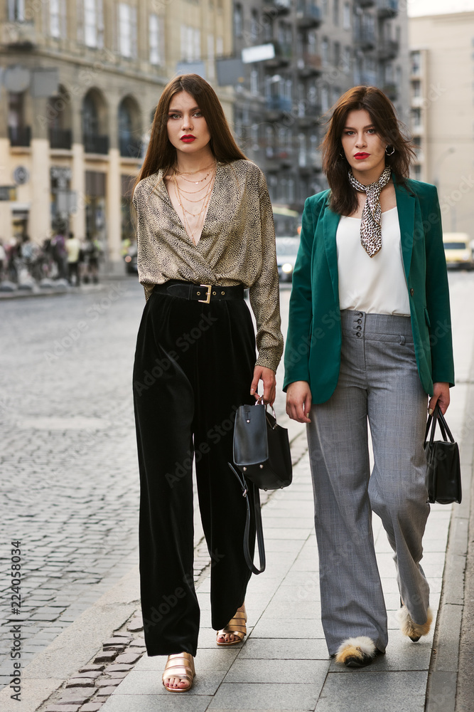 Outdoor full body portrait of two young beautiful fashionable women wearing stylish  trendy clothes, shoes and accessories walking in street of european city.  Street fashion concept Stock Photo
