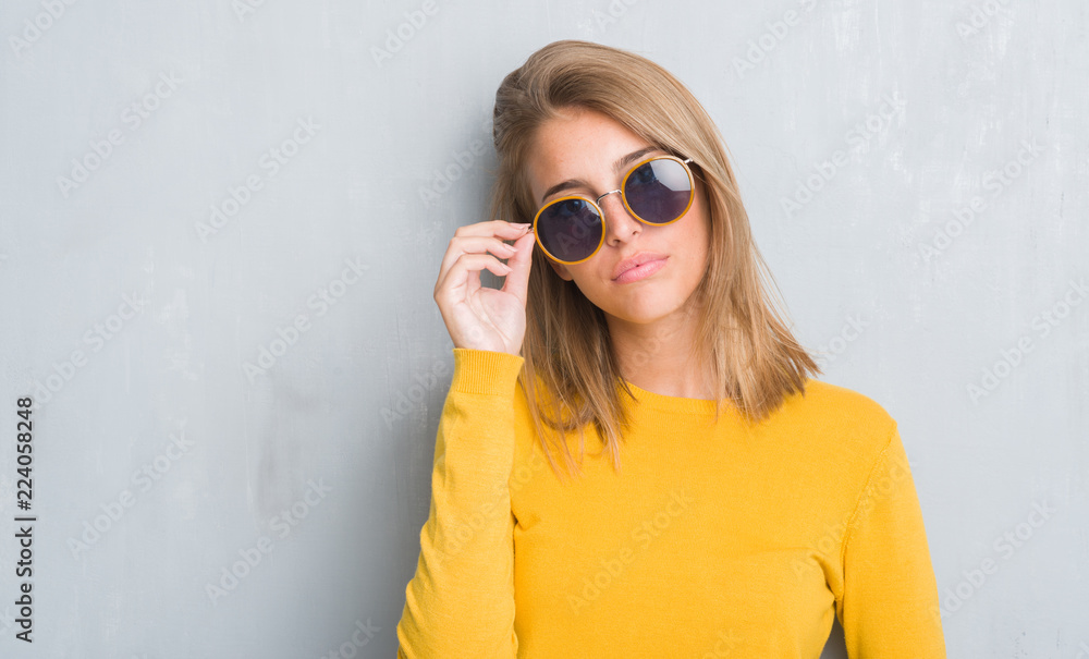 Beautiful young woman standing over grunge grey wall wearing retro sunglasses with a confident expression on smart face thinking serious Beautiful young woman standing over grunge grey wall wearing retro sunglasses with a confident expression on smart face thinking serious