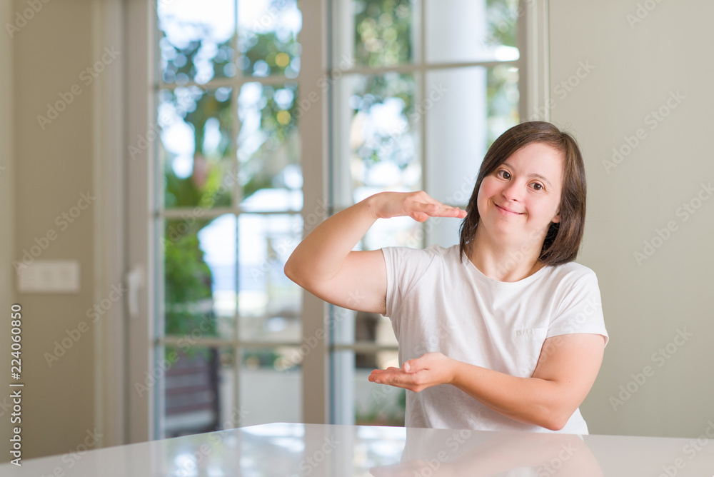 Down syndrome woman at home gesturing with hands showing big and large size sign, measure symbol. Smiling looking at the camera. Measuring concept.