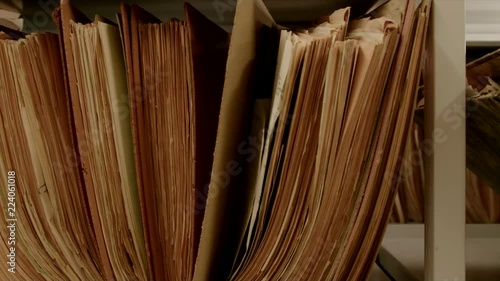 Camera movement along a file shelf. The files are old. In the background of the archive are even more shelves.
