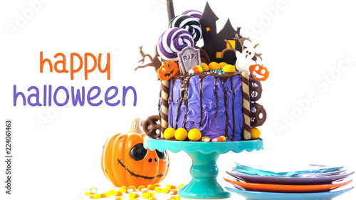 On trend Halloween candyland fantasy novelty drip cake on white background with Happy Halloween text greeting.