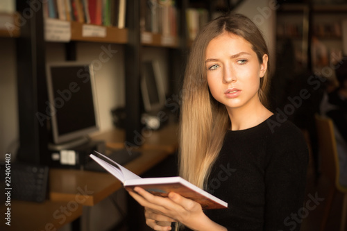 Serious young teenage girl student sitting in library reading book. Looking aside doing homework.