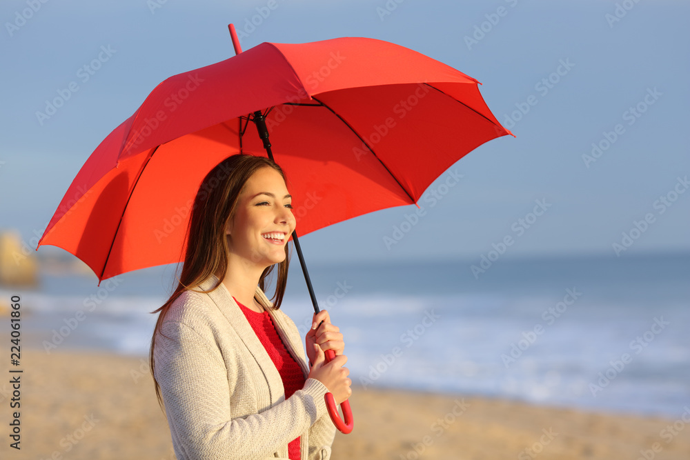 Happy girl with red umbrella watching sunset on the beach