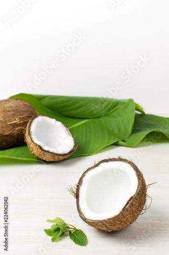 Ripe coconut and tropical leaves on a light wooden background, minimal flat lay style. Creative summer and food concept. Tropical fruit