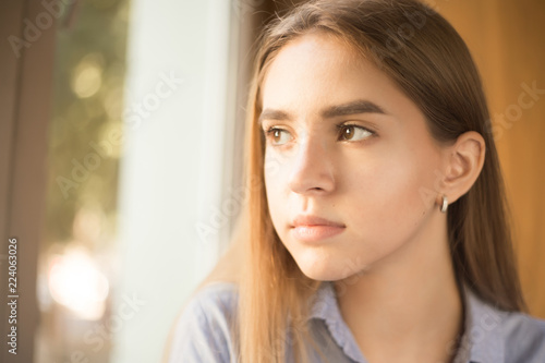 Beautiful concentrated young teenage girl student sitting in library looking at window.