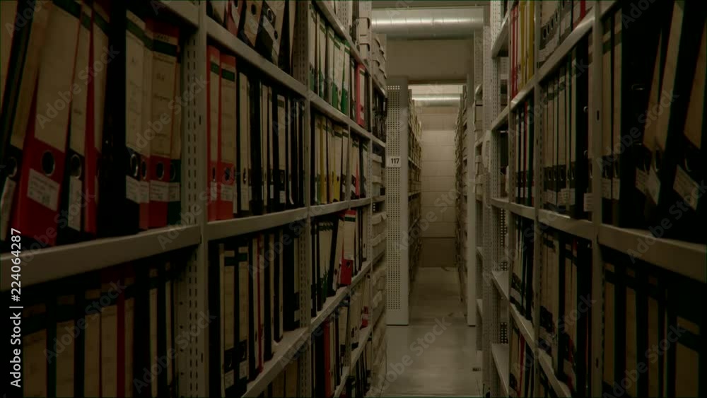 Slow camera movement between two archive shelves filled with folders. The image can be used for the integration of archive texts in films and reports. Thanks to the 50 frames it can be slowed down. Slow camera movement between two archive shelves filled with folders. The image can be used for the integration of archive texts in films and reports. Thanks to the 50 frames it can be slowed down.