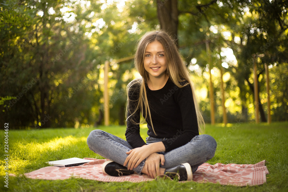 Happy cheerful girl student sitting in the park outdoors on grass looking camera. Happy cheerful girl student sitting in the park outdoors on grass looking camera.