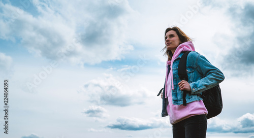 tourist traveler with black backpack on background mountain, hiker looks up at blue sky clouds, girl enjoying nature panoramic landscape in trip, relax holiday mockup concept in trekking trip