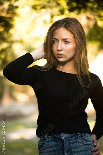 Beautiful serious concentrated girl student posing in the park outdoors on grass looking aside.