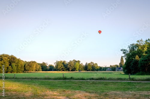 Colorful air balloon is riding above a Dutch farm landscape in the summer month of June. This landscape is near the small city of Delden in a region called Twente, in the province of Overijssel