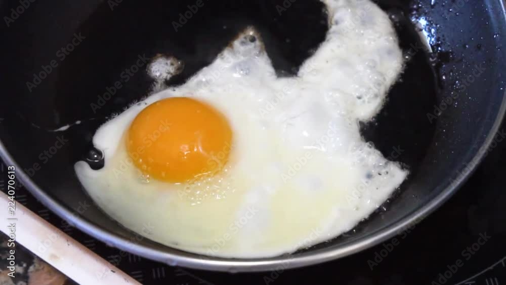 Cooking egg in black pan, someone hand adding salt Cooking egg in black pan, someone hand adding salt