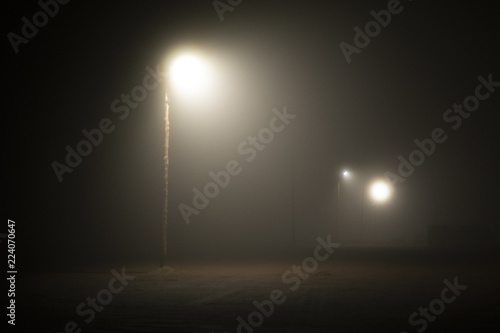 Street lights foggy misty night lamp post lanterns deserted road. Lonely street at night in the light of lanterns. foggy night parking lot