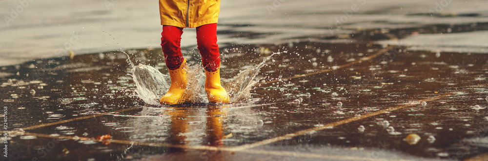 Fototapeta premium legs of child with rubber boots jump in puddle on autumn walk