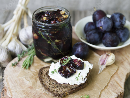 Glass jar with dried plums and fresh rosemary on wooden serving board, selective focus.