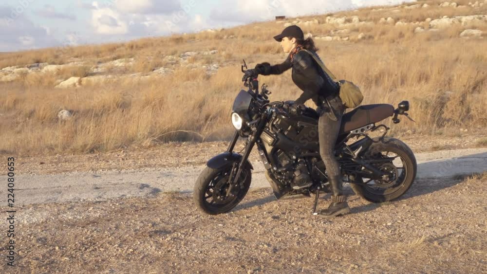 Young biker woman sits down on a motorcycle and leaves Ride on the old desert road Young biker woman sits down on a motorcycle and leaves Ride on the old desert road