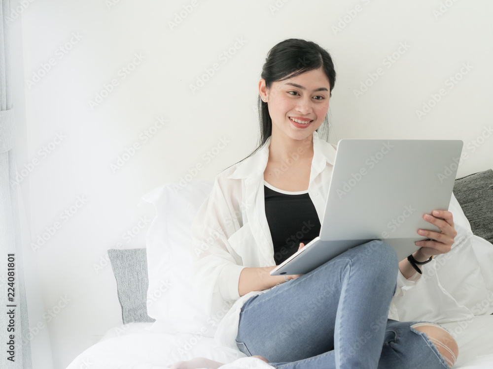 Happy Asian woman using laptop on bed, relaxing at home. Happy Asian woman using laptop on bed, relaxing at home.