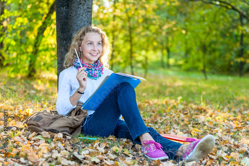 Obraz na płótnie Teen student woman sitting on lawn in park with books and notebook and writes