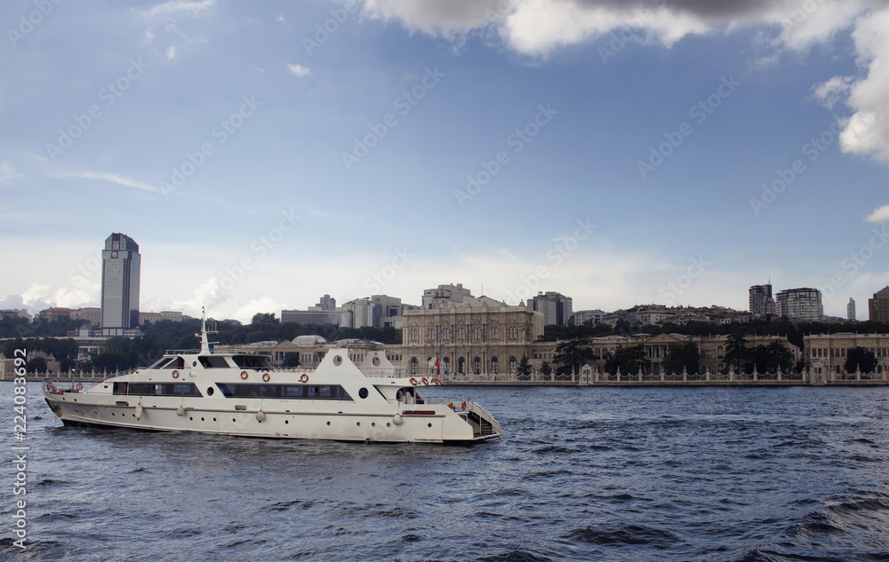 View of a white luxury yacht on Bosphorus, old historical buildings on the European side in Istanbul.