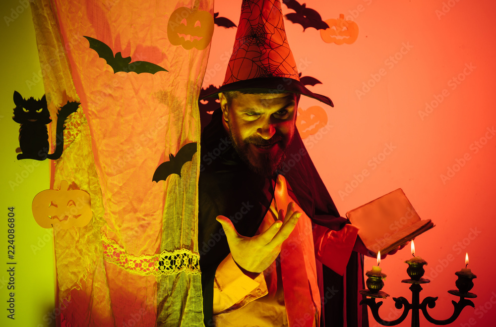 Fototapeta premium Happy father on halloween background with magik book. Man pronounces a spell, reads a magic book. Man Horror faces. Happy halloween. Horror faces. People wearing hallowwen carnival costumes.