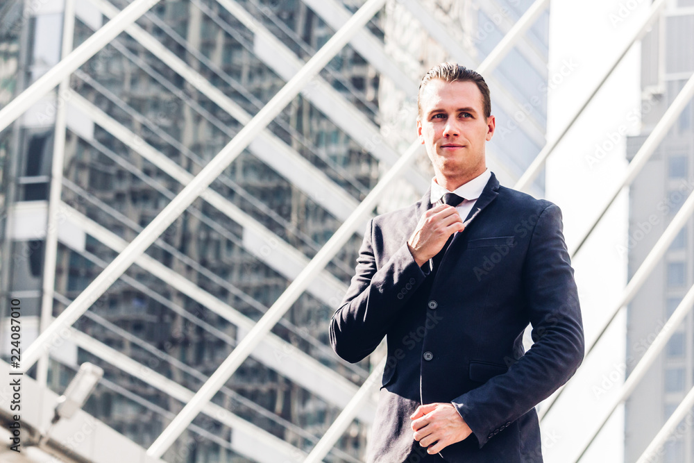 Portrait of handsome businessman in black suit standing outdoors on modern city background Portrait of handsome businessman in black suit standing outdoors on modern city background