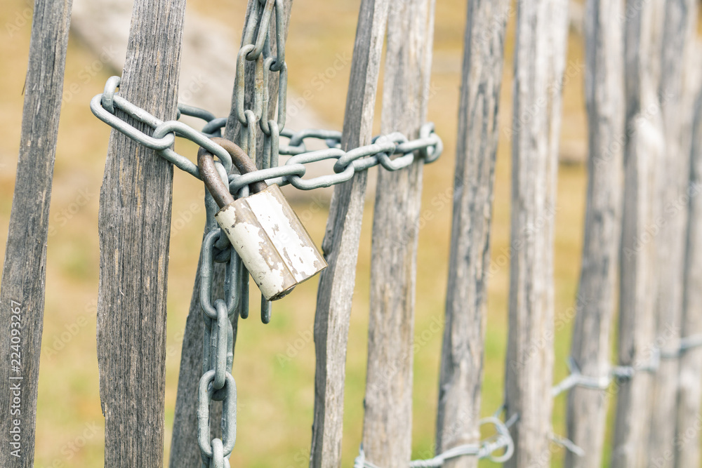Wooden fence closed by chain with padlock in countryside, close-up