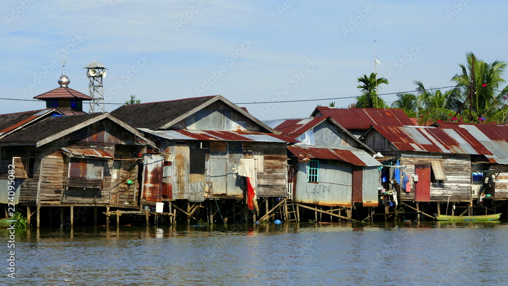 Fototapeta premium einfache Hütten stehen auf Pfählen im Fluss Martapura und spiegeln sich im Wasser