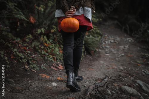 woman walking along a forest path holding an orange pumpkin