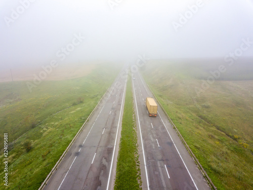 Aerial view from the drone a misty morning on the road with a truck around the field.