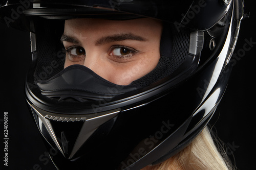 Close up portrait of Caucasian female motorcycle racer with happy eyes wearing black modern safety helmet, going to competition, feeling excited. Speed, extreme, danger and activity concept