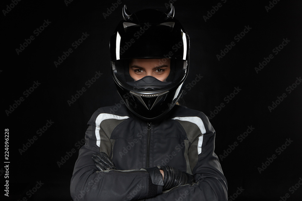 Motorcycle sports, extreme, competition and adrenaline. Active young female racer wearing protective helmet and uniform going to participate in road racing or motorcross, crossing arms on her chest