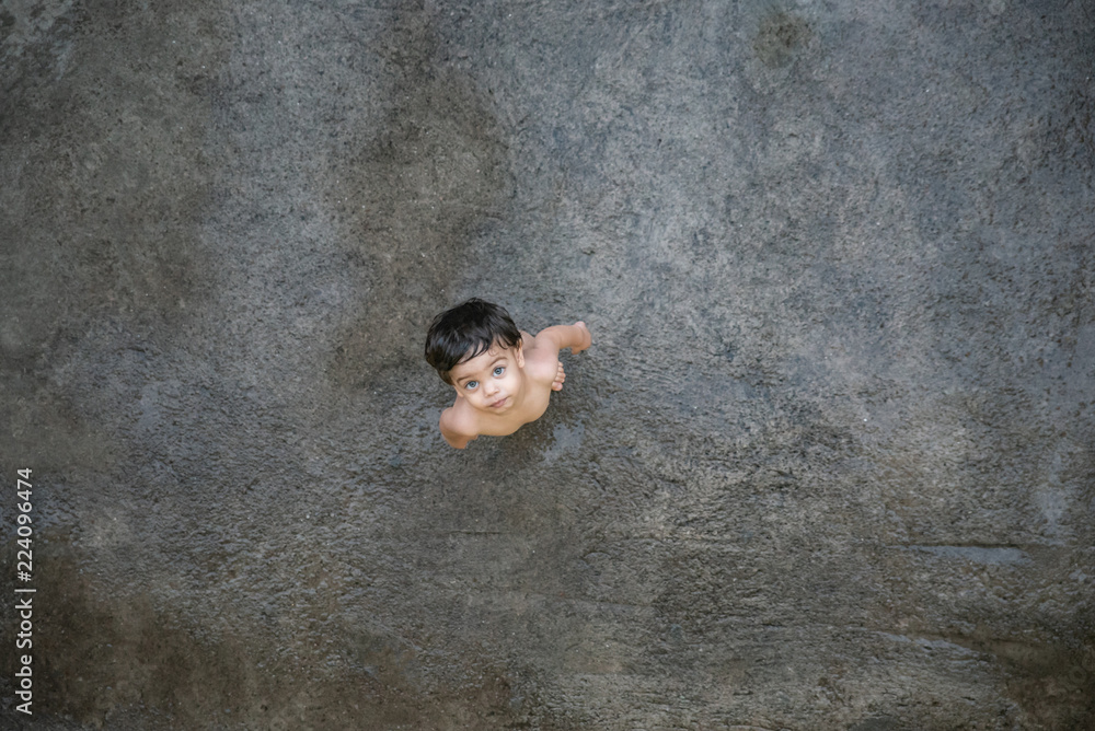 Cute baby boy toddler - naked on a wet gray floor - Top view