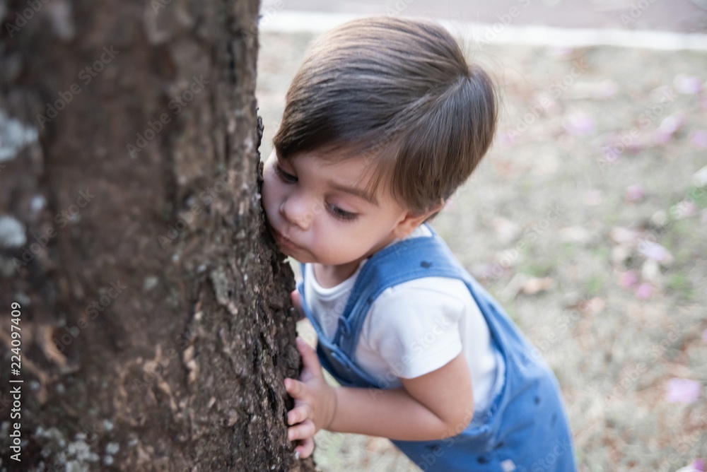 Cute baby boy toddler with romper - In the garden hugged on the tree. Cute baby boy toddler with romper - In the garden hugged on the tree.