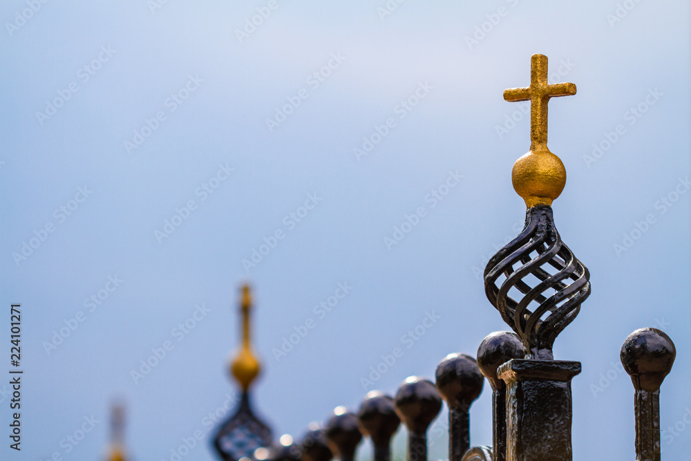 Forged metal fence decorated with gold crosses near the Orthodox Church. Blue sky background, closeup, selective focus Forged metal fence decorated with gold crosses near the Orthodox Church. Blue sky background, closeup, selective focus