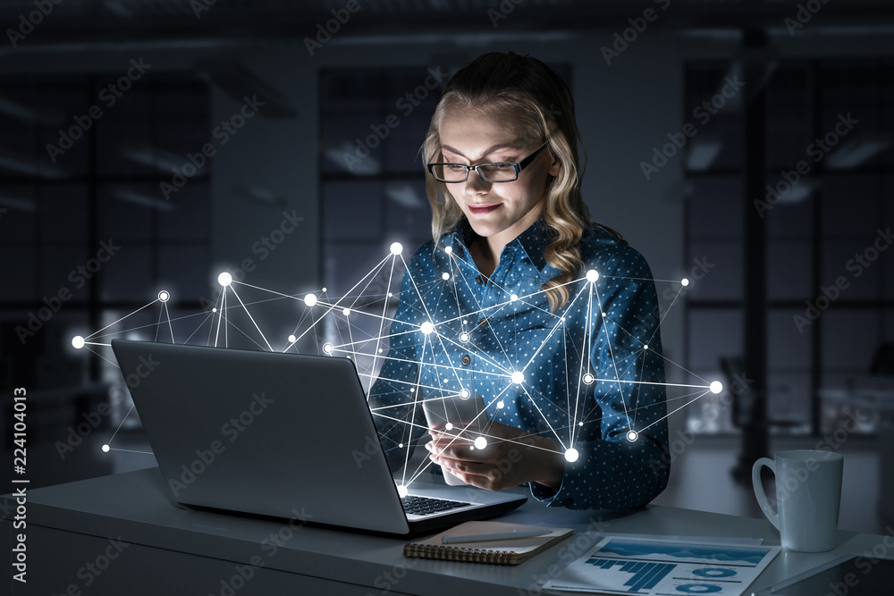 Attractive blonde wearing glasses in dark office using laptop. M