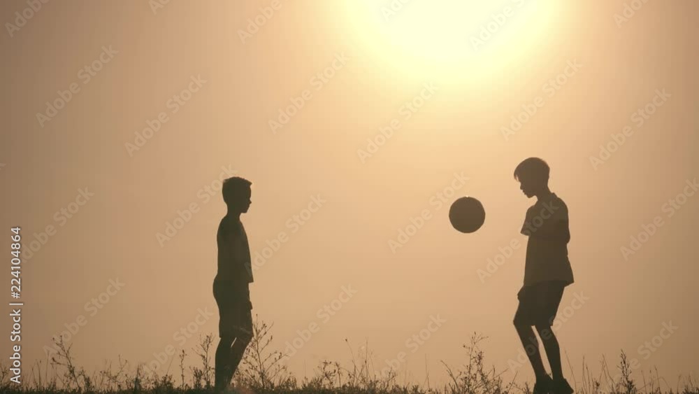 Two boys playing soccer at sunset. Silhouette of children playing with a ball at sunset. The concept of a happy family Two boys playing soccer at sunset. Silhouette of children playing with a ball at sunset. The concept of a happy family