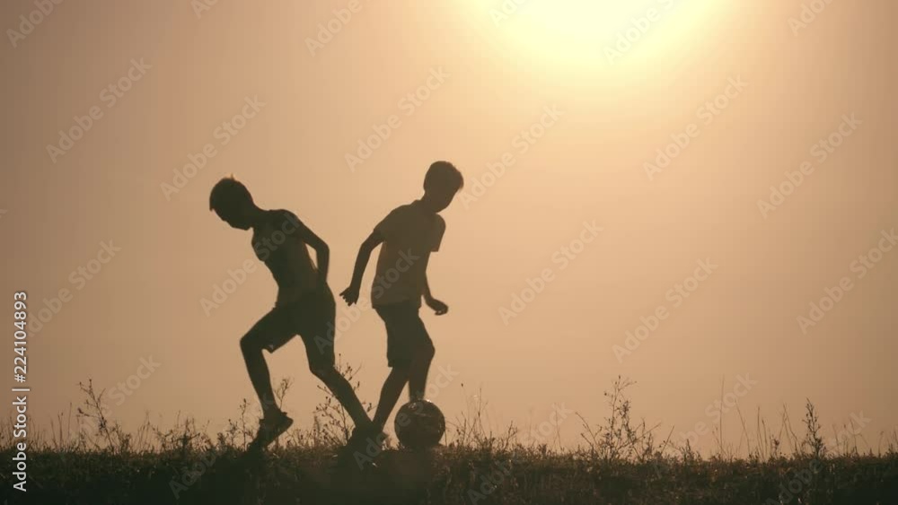 Two boys playing soccer at sunset. Silhouette of children playing with a ball at sunset. The concept of a happy family Two boys playing soccer at sunset. Silhouette of children playing with a ball at sunset. The concept of a happy family