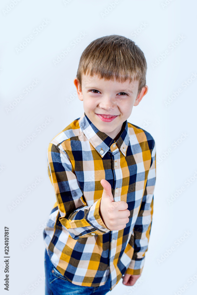 Little boy in plaid shirt on white background shows thumb up with hand and rejoices. Concept - everything is cool. Little boy in plaid shirt on white background shows thumb up with hand and rejoices. Concept - everything is cool.