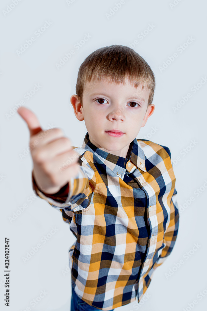 Little boy in plaid shirt on white background shows thumb up with hand and rejoices. Concept - everything is cool. Little boy in plaid shirt on white background shows thumb up with hand and rejoices. Concept - everything is cool.
