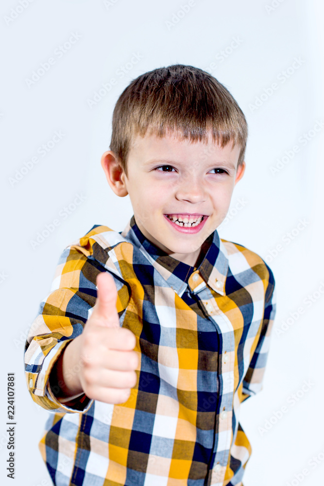 Little boy in plaid shirt on white background shows thumb up with hand and rejoices. Concept - everything is cool. Little boy in plaid shirt on white background shows thumb up with hand and rejoices. Concept - everything is cool.