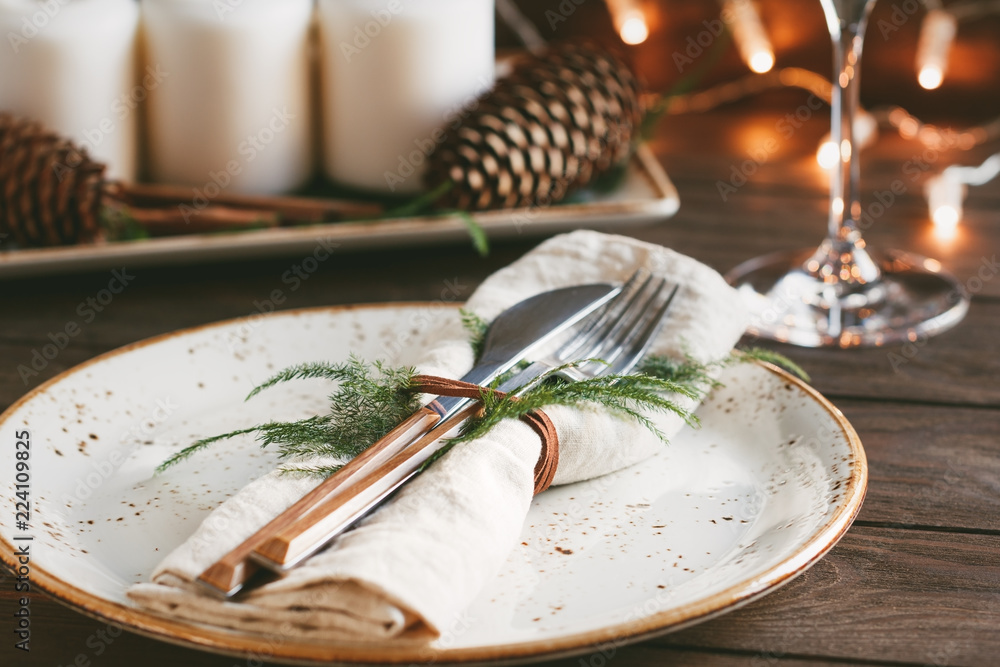 Thanksgiving table setting among white candles and cones. Ceramic plate with fork and knife on a linen napkin. The concept of a festive dinner. - obrazy, fototapety, plakaty 