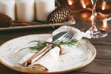 Thanksgiving table setting among white candles and cones. Ceramic plate with fork and knife on a linen napkin. The concept of a festive dinner.