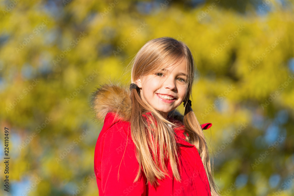 Naklejka premium Fall fashion. Girl smiling face cute hairstyle fashionable fall coat with hood and fur. Kid girl wear coat for fall season. Child cheerful walking wearing warm bright coat or jacket fall sunny day