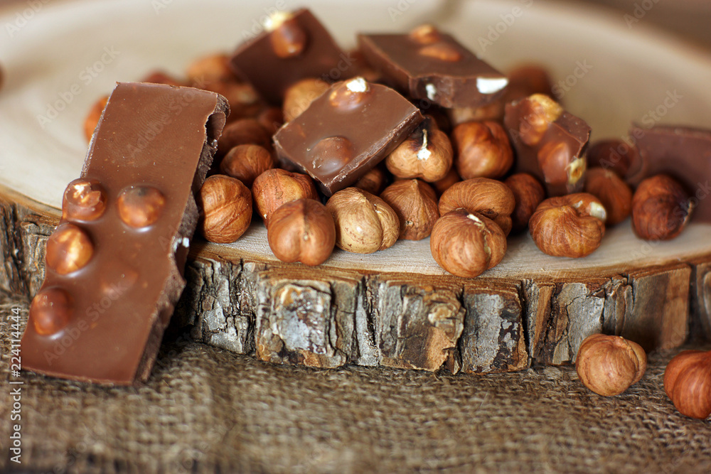 Tile of milk chocolate with hazelnuts next to a handful of nuts Tile of milk chocolate with hazelnuts next to a handful of nuts