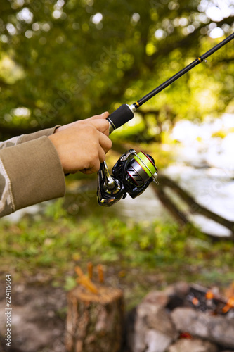 A fisherman with a fishing rod. Close-up of a hand holding a spinning rod and twisting a coil. Colorful view, blurred background, selective focus.