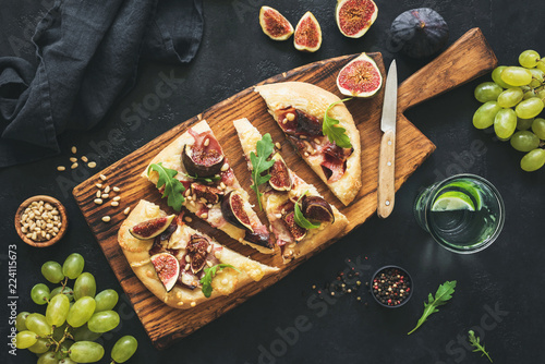 Flatbread with figs, prosciutto, grapes, arugula on wooden serving board. Top view, toned image. Sliced pizza