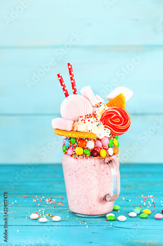 Extreme milkshake. Freakshake. Pink strawberry freakshake with sweets on blue background. Selective focus. Overshake
