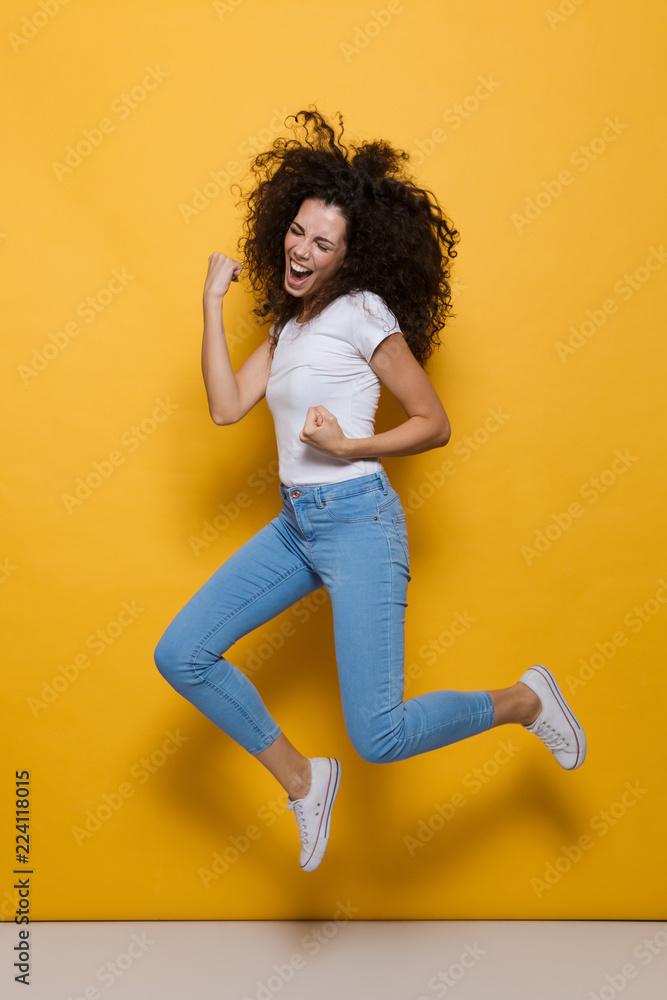 Full length photo of young woman 20s with curly hair having fun and jumping, isolated over yellow background Full length photo of young woman 20s with curly hair having fun and jumping, isolated over yellow background