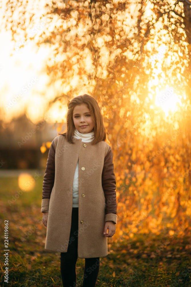 A teenage girl stands in a coat on the background of golden tree. Yellow and orange color of autumn A teenage girl stands in a coat on the background of golden tree. Yellow and orange color of autumn
